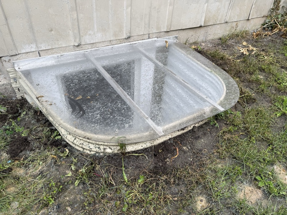 Clear polycarbonate egress window well cover installed against the foundation