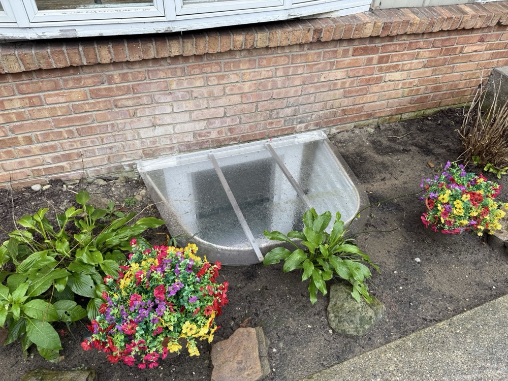 Egress window well and cover finished into the landscaping of a brick home