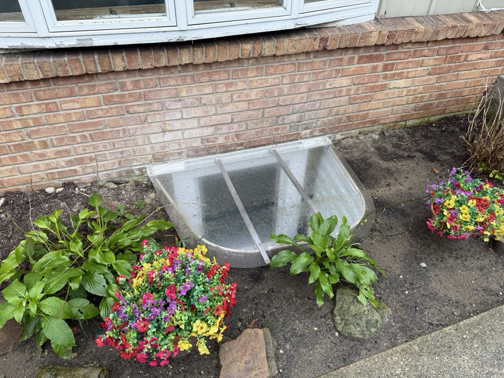 Covered egress window well alongside restored planting beds