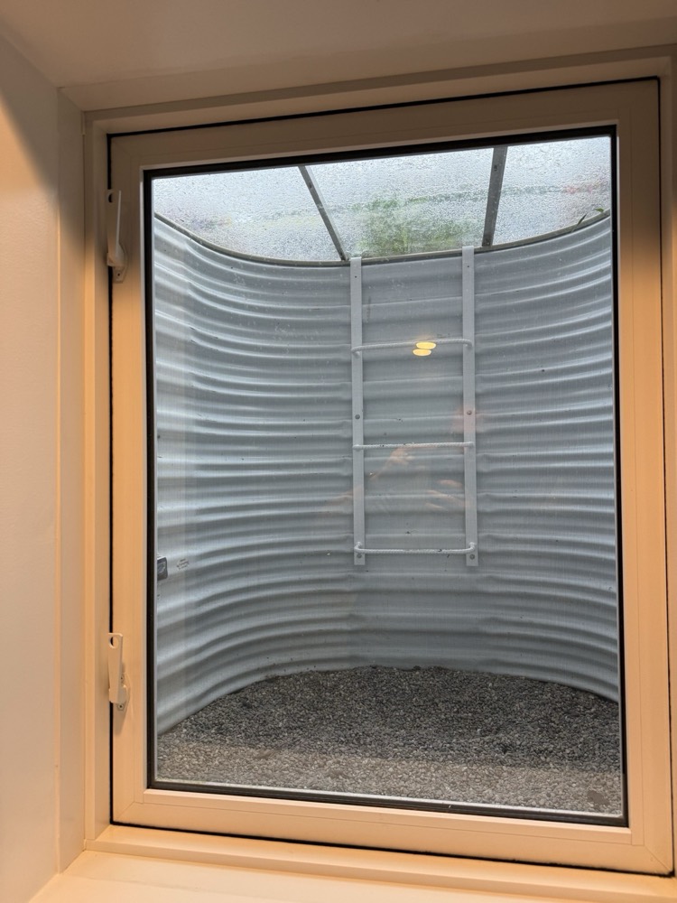 Close view of a finished basement egress window showing the well and escape ladder